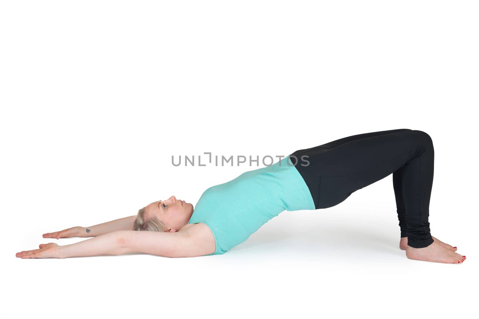Full body view of a young blonde woman doing yoga exercises against a white background with a slight shadow