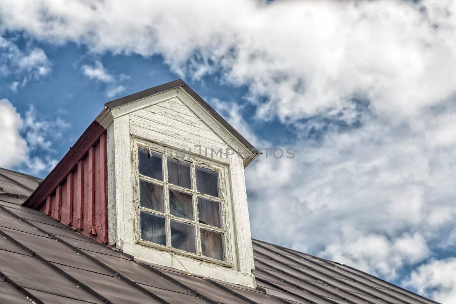 Weathered Window on Roof with a cloudy sky.