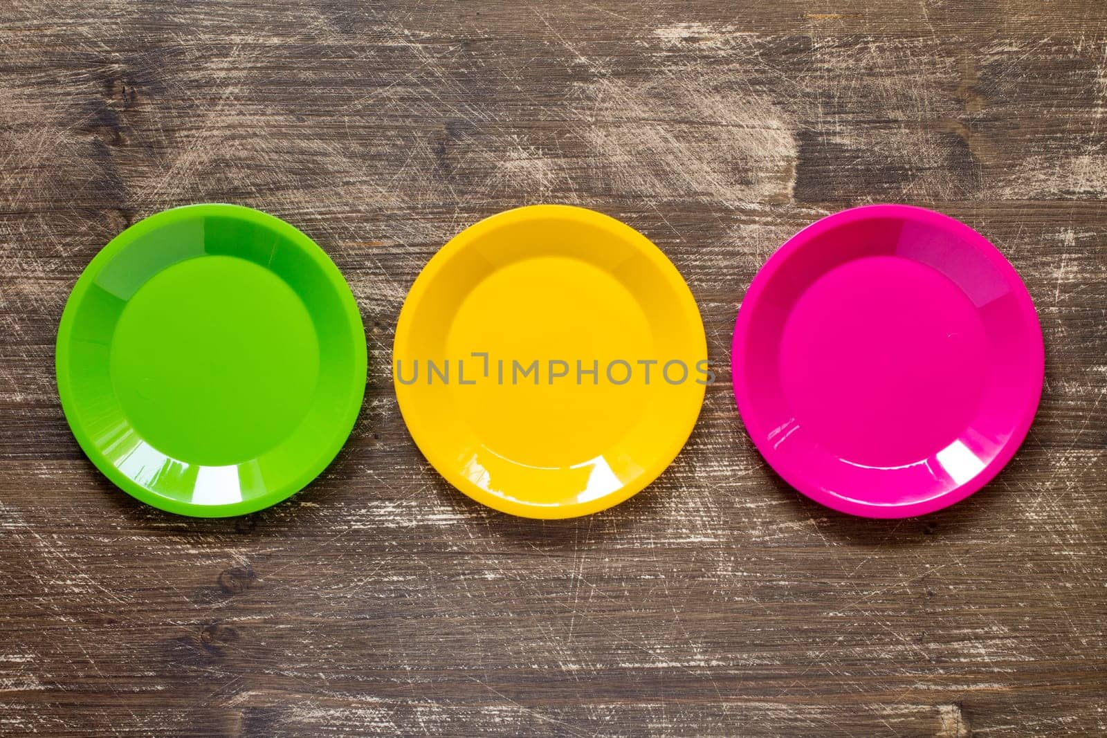 Green, yellow and pink color plates set  on wooden background