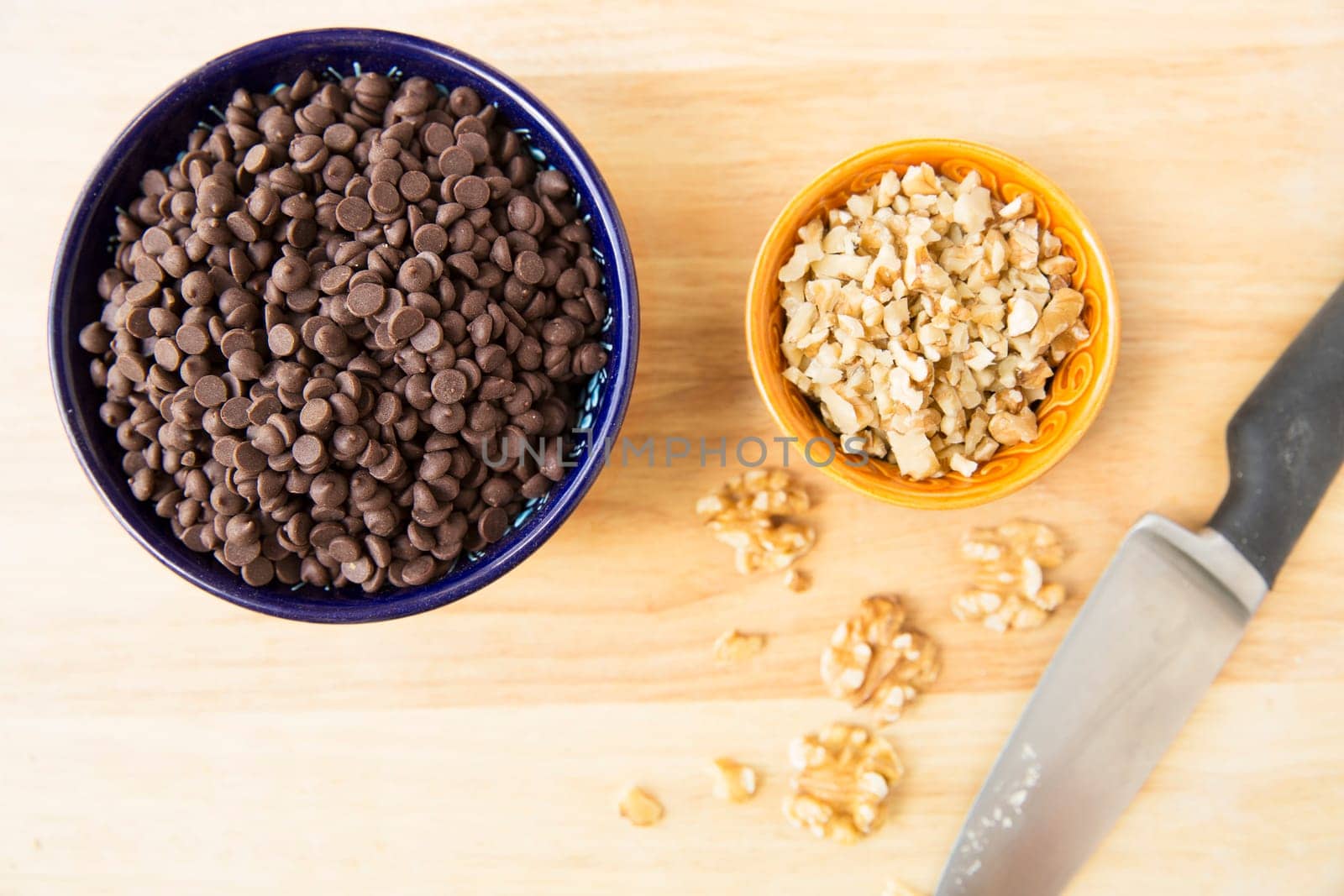 Chocolate chips and chopped walnuts in bowl with knife, viewed from above.