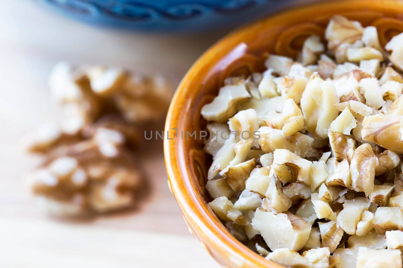 Chopped walnut pieces in an orange bowl on table.