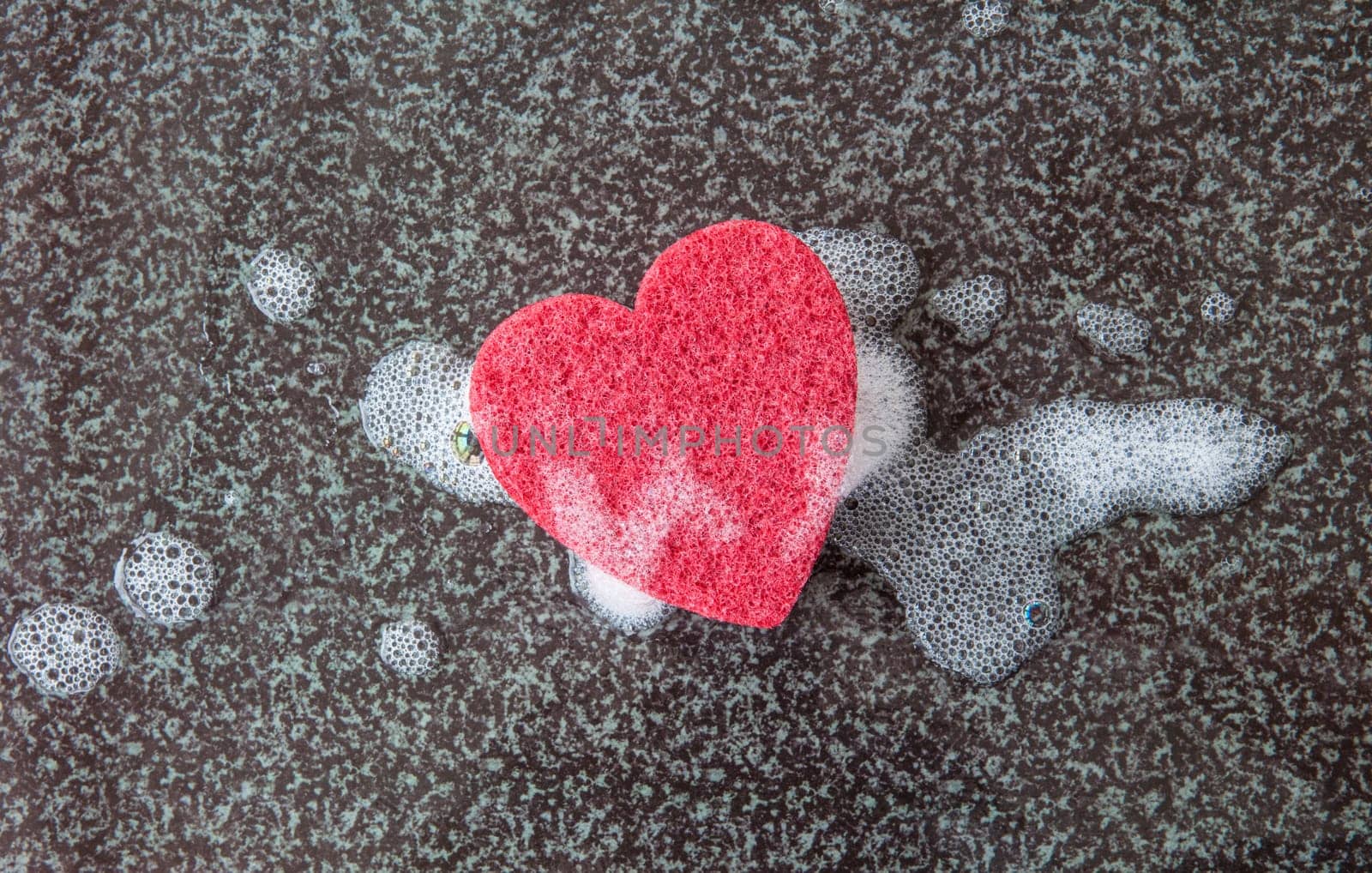 Red sponge in heart shape with detergent on a dark background