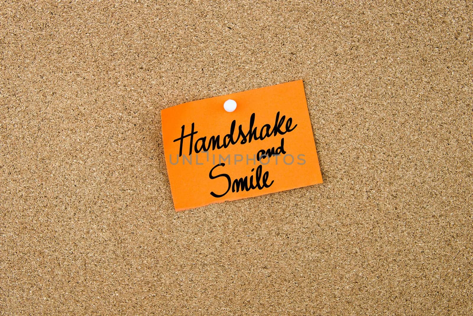 Handshake and Smile written on orange paper note note pinned on cork board with white thumbtack, copy space available