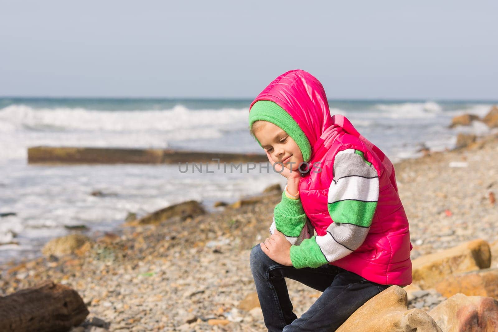 Girl sitting on the rocky beach and the sea happily lost in thought looking down