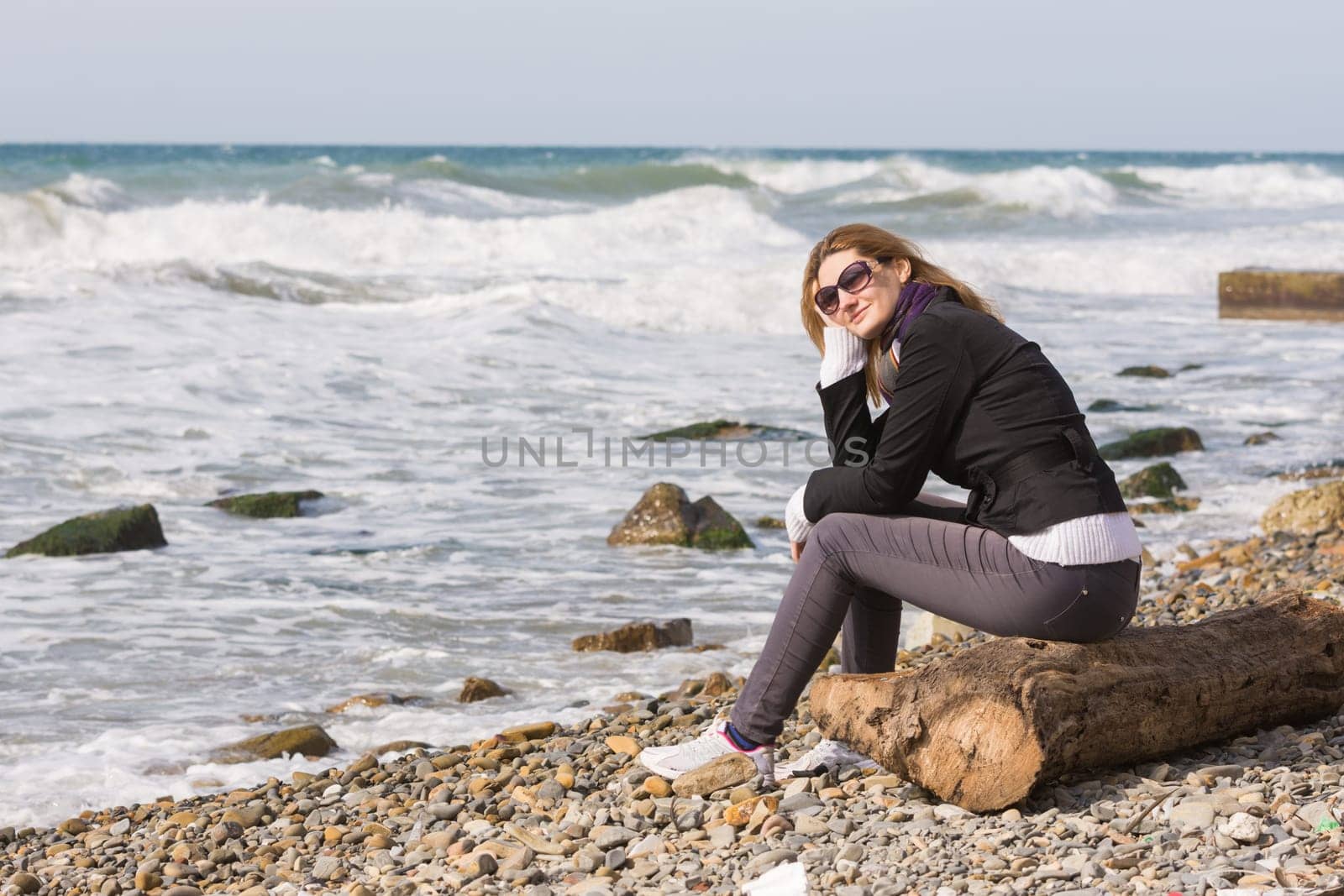 Happy girl with glasses sitting on a log on a rocky beach ocean