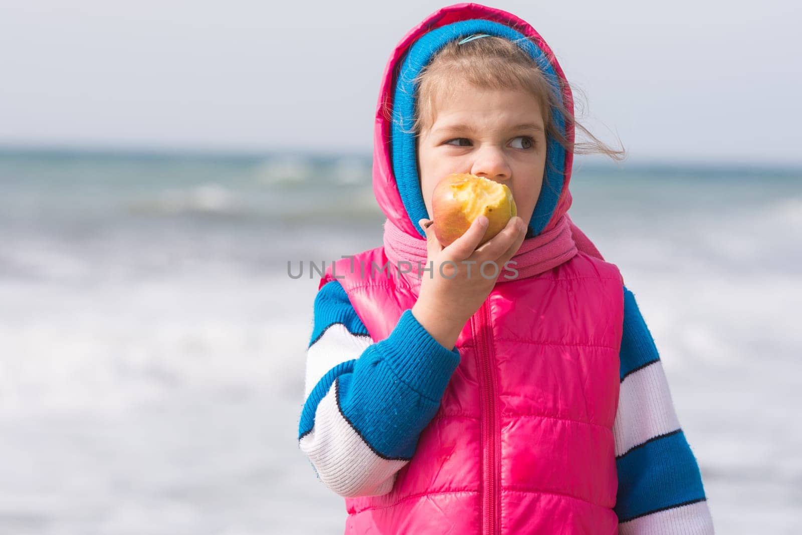 Five-year girl eating an apple on the background of the sea coast