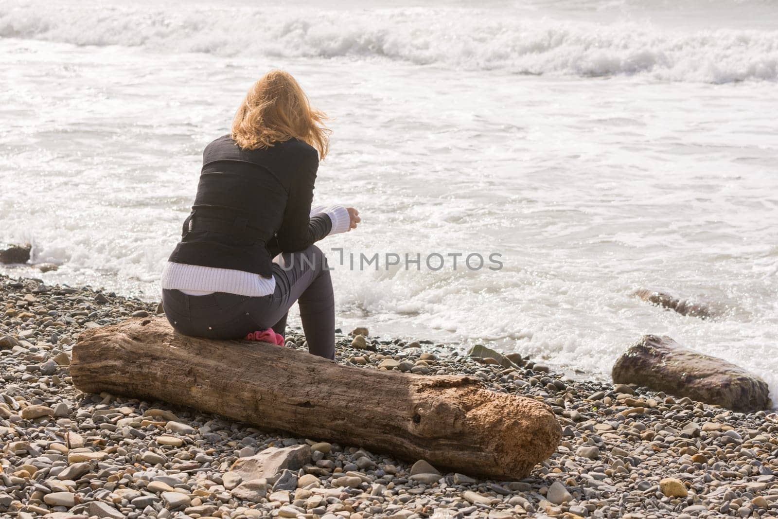 Girl sitting on the log on the coast and looks at sea