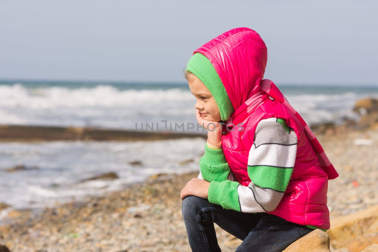 Girl sitting on the rocky beach and the sea head on his hand looking to the frame