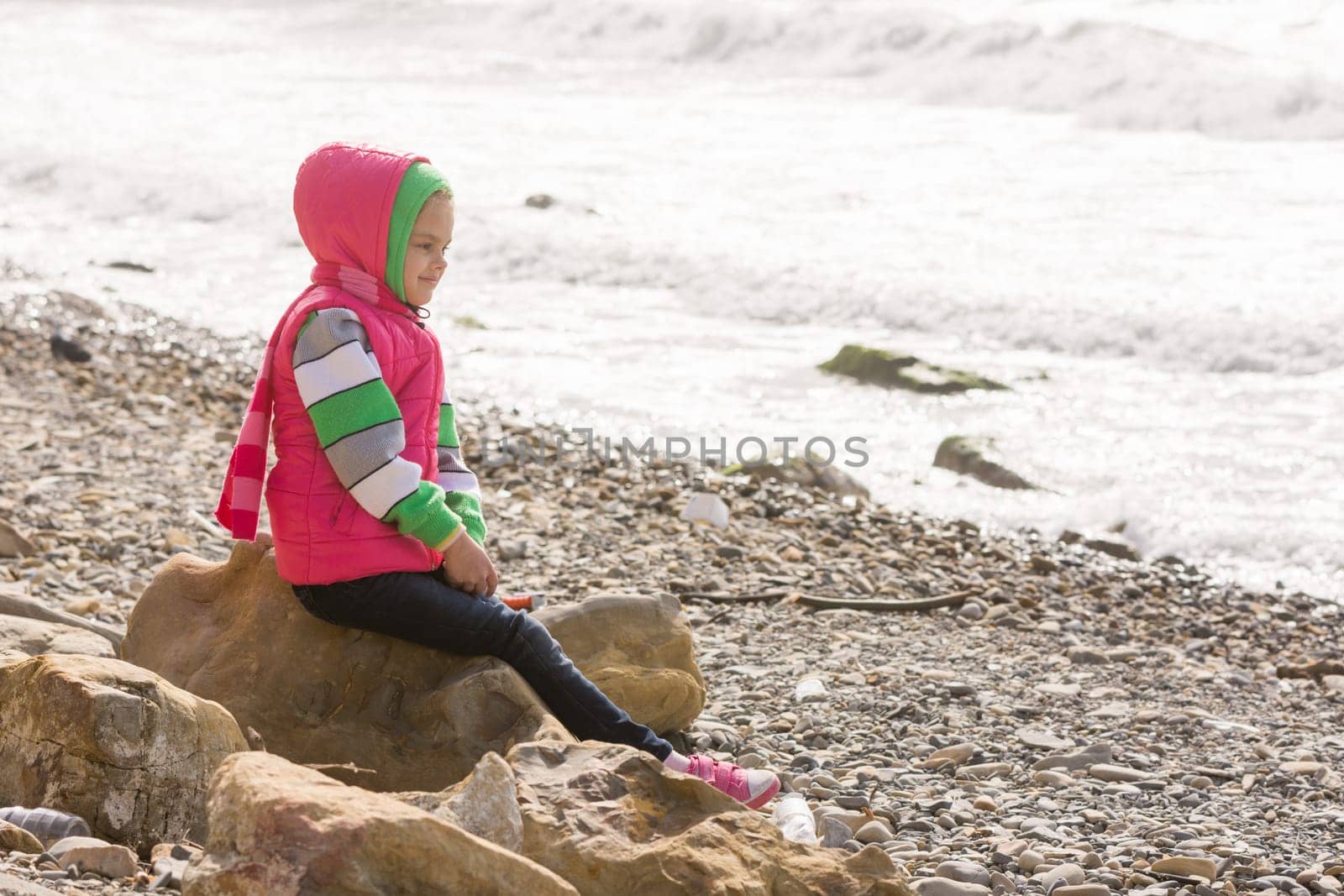 Happy girl sitting on a rock on the sea coast and looking into the distance