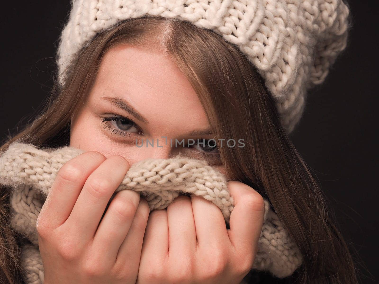 Close up portrait of a beautiful teenage girl dressed with wool cap and scarf on a gark background