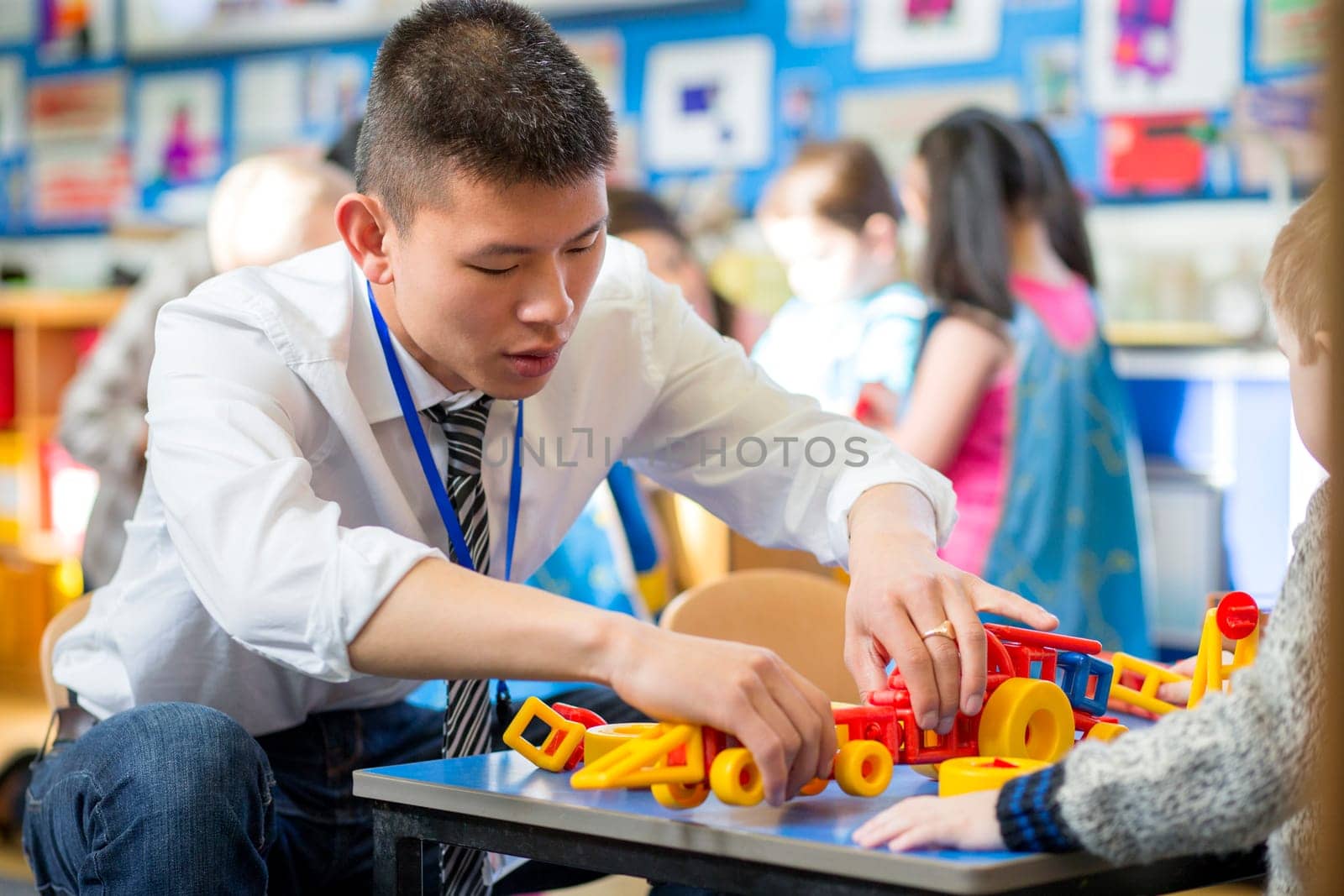 Nursery teacher is helping one of his students to make a car with building blocks.