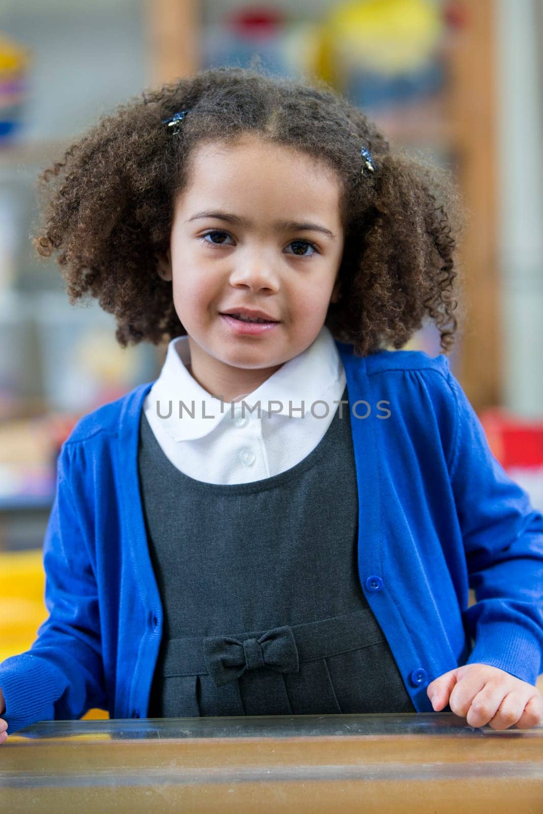 Portrait of a school girl. She is wearing a blue cardigan and smiling at the camera.