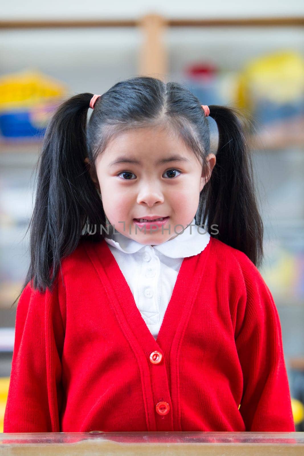 Portrait of a school girl. She is wearing a red cardigan and smiling at the camera.