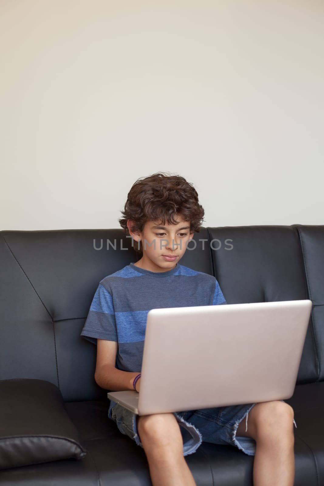 Latino boy sitting on sofa with laptop computer.