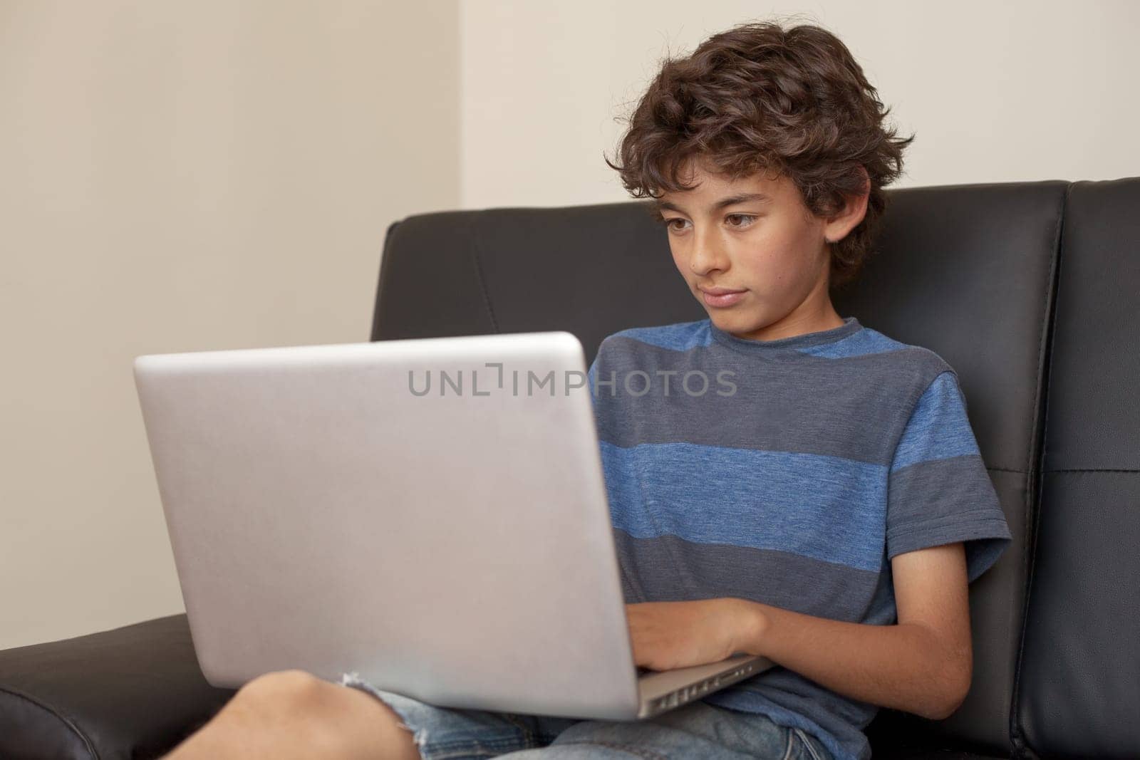 Latino boy sitting on sofa with laptop computer.