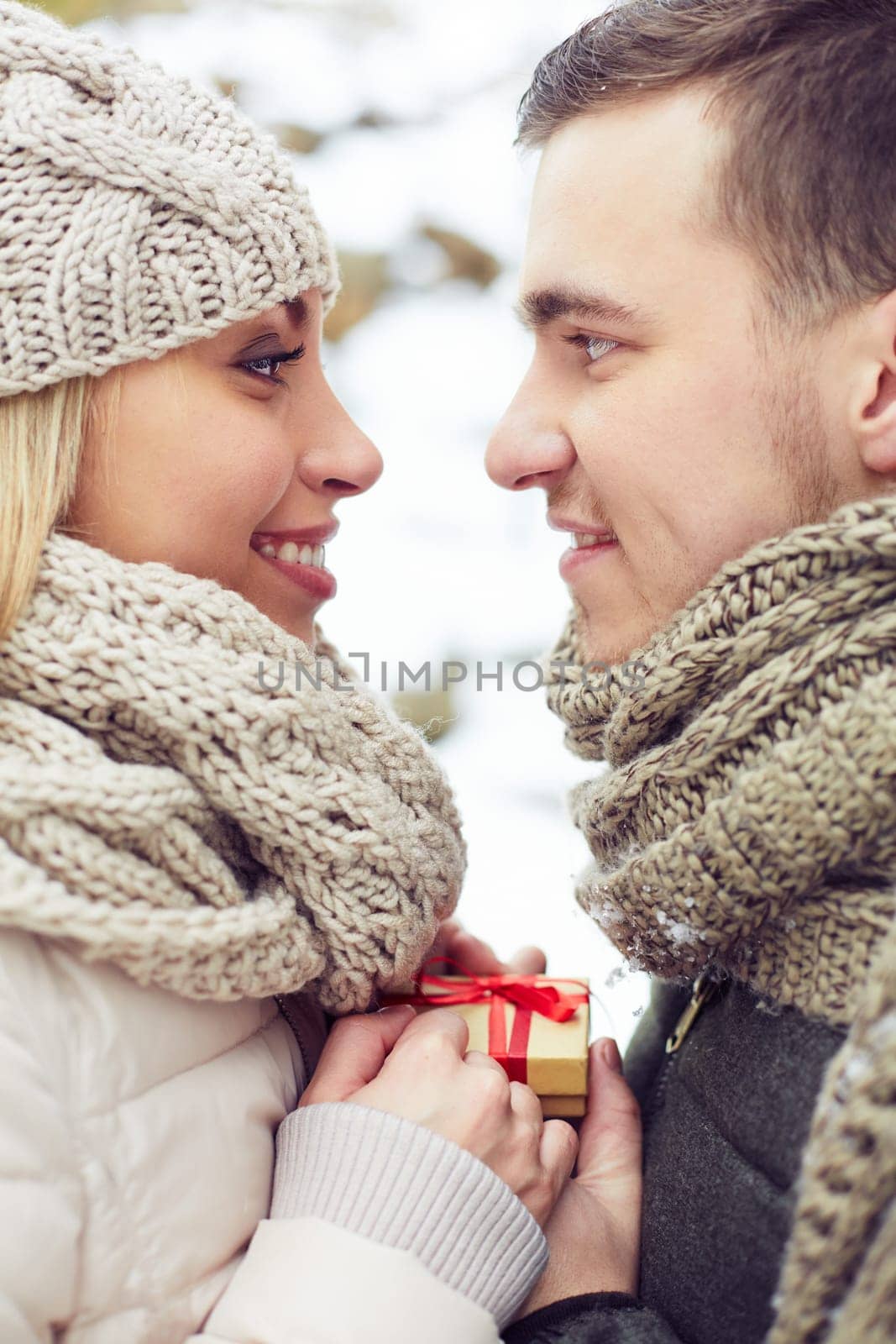 Young amorous man giving small present to his girlfriend and both looking at one another