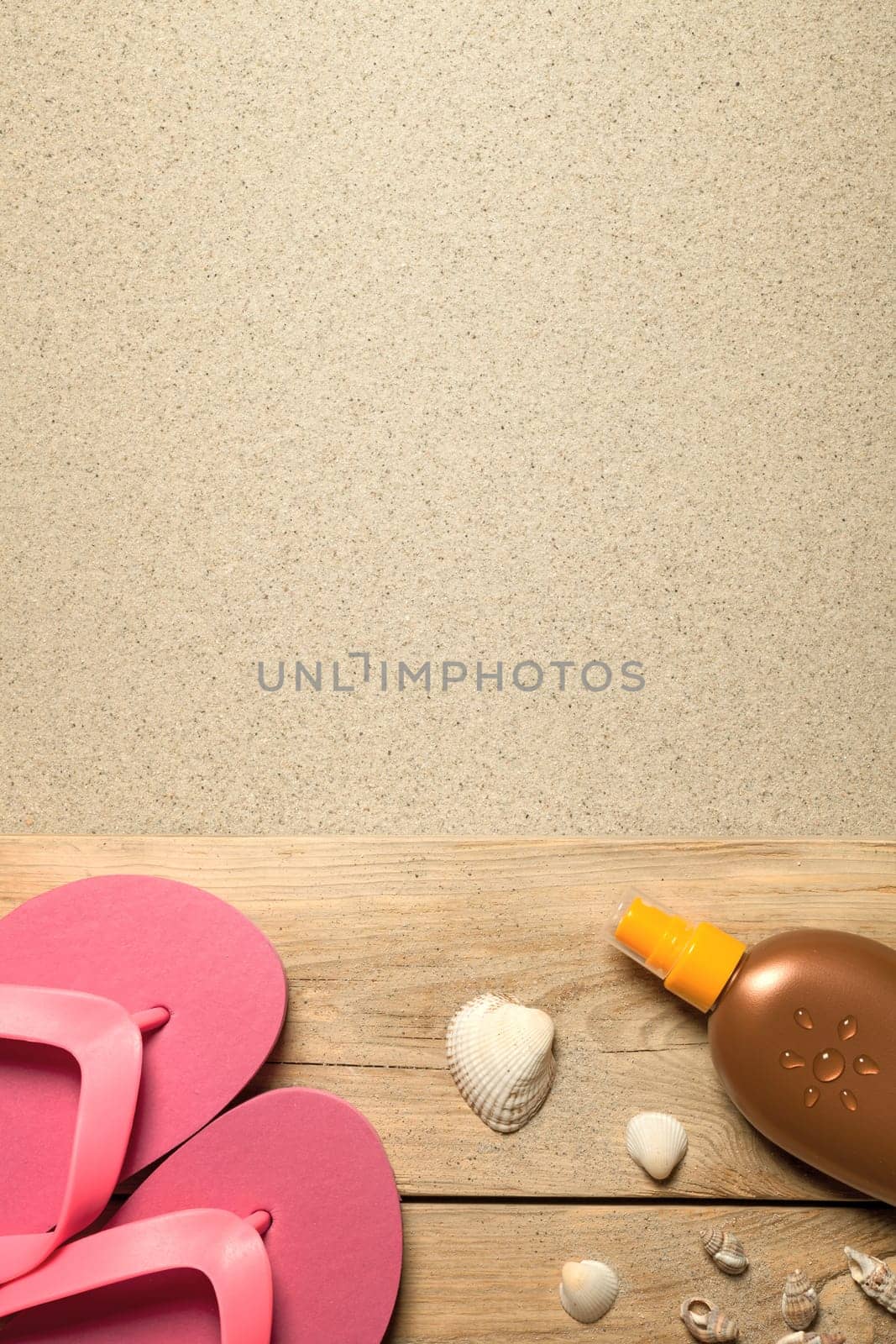 summer concept with pink flip flops,shells and suntan oil on sandy beach. top view