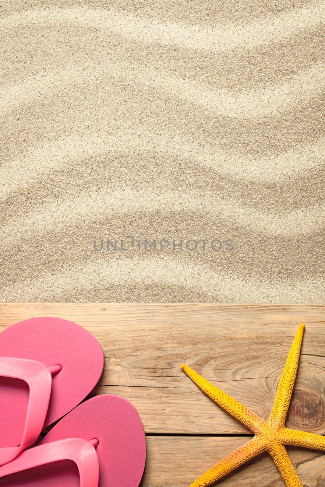 summer concept with pink flip flops and yellow starfish on sandy beach