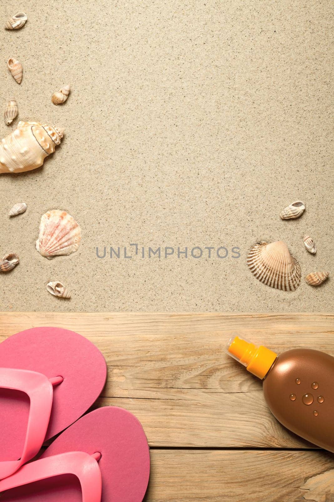 summer concept with pink flip flops,suntan oil and shells on sandy beach. top view