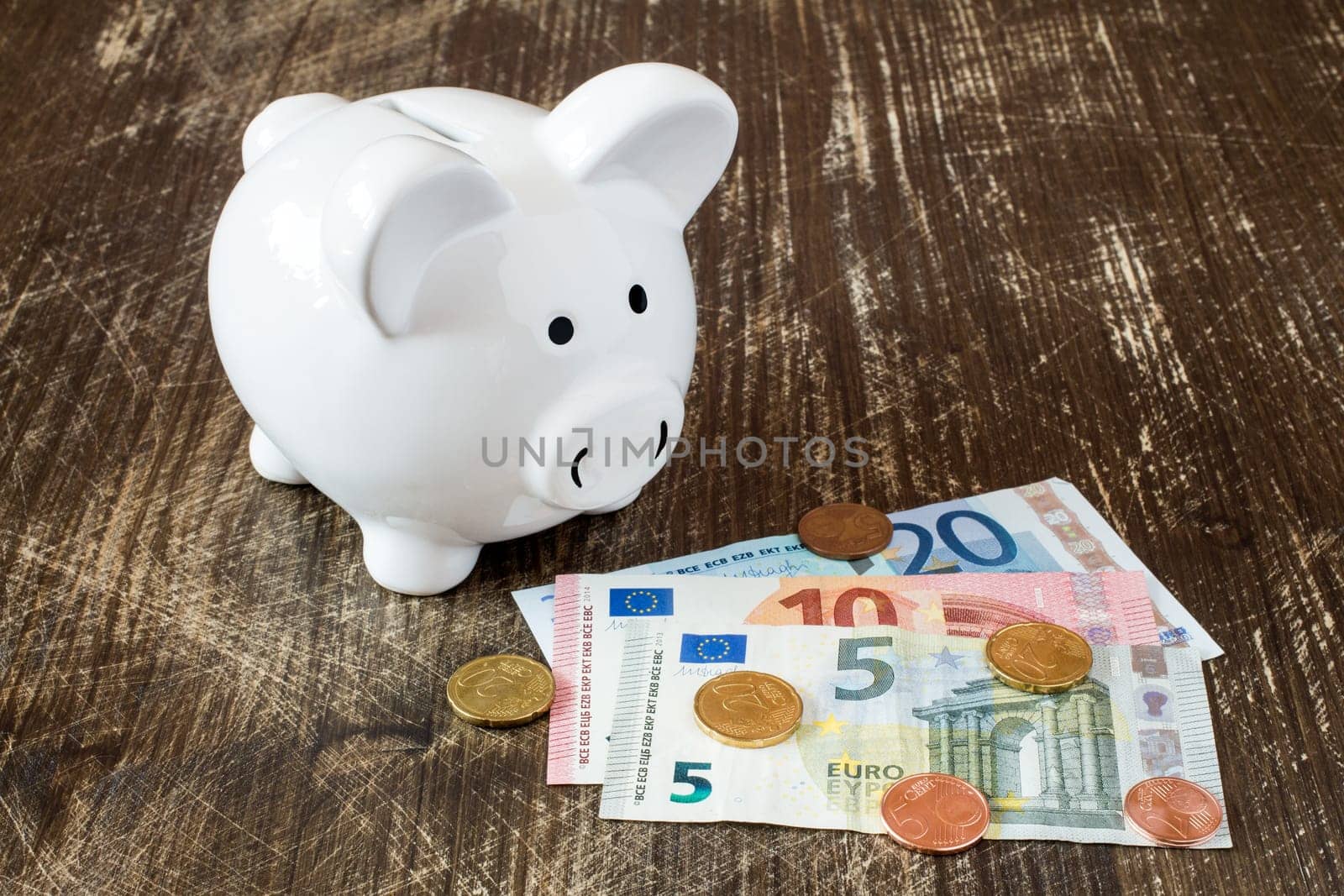 Piggy bank with Euro notes and coins on wooden background