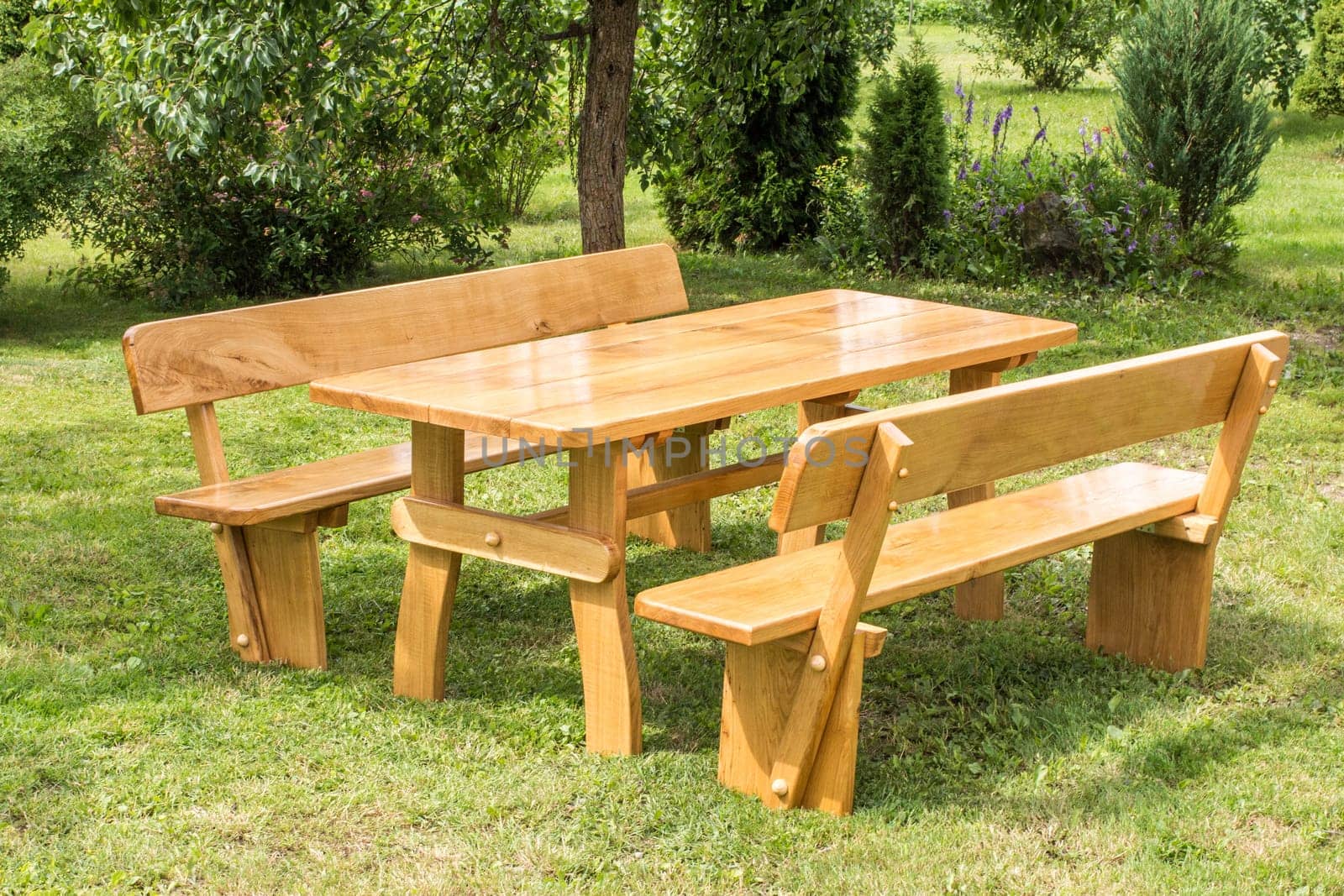 Wooden set of table, benches with backrests on green grass lawn. Vacation place in garden. Summer leisure time.