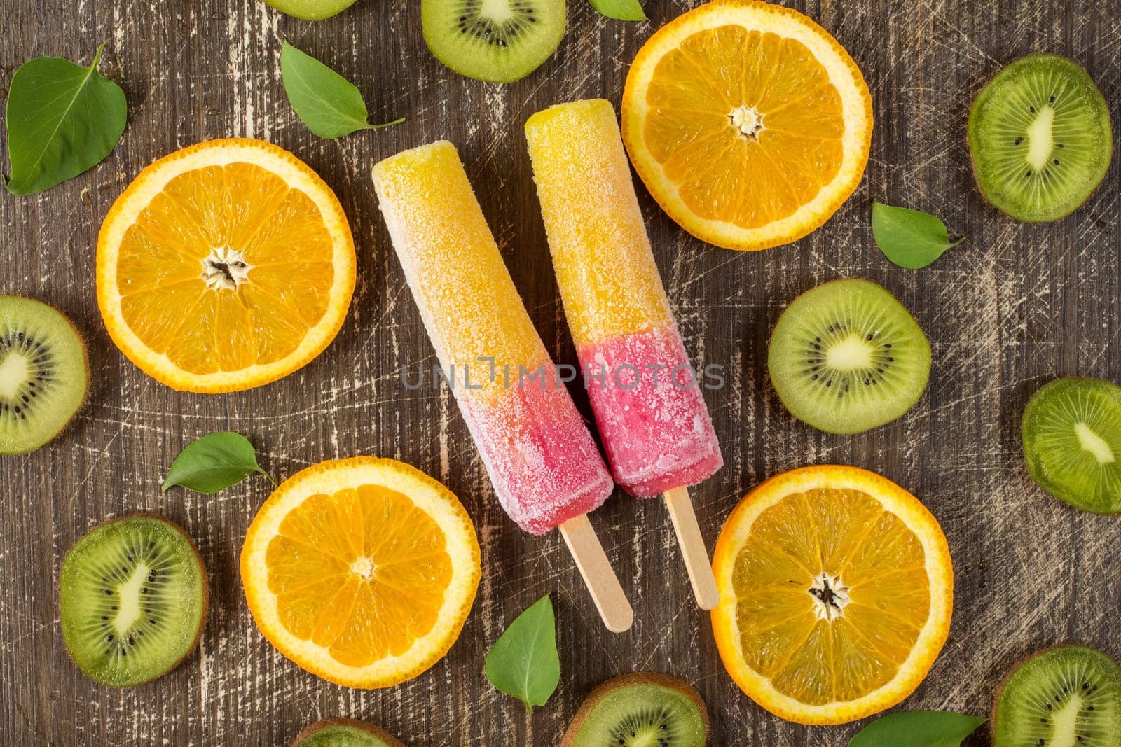 Popsicles with sliced orange and kiwi fruit on wooden background. Top-view.