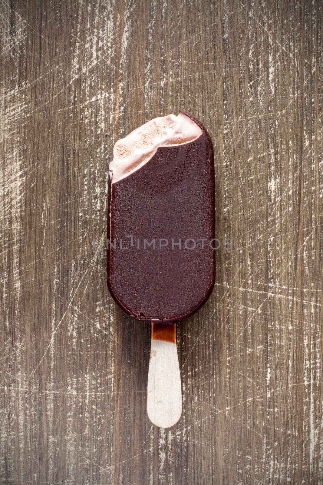 Bitten chocolate covered vanilla ice cream bar on a wooden stick