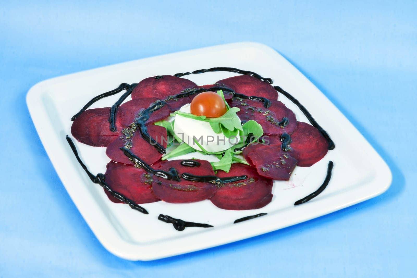 Modern food on a white plate and blue background - Thin slices of beetroot with goat cheese and balsamic reduction