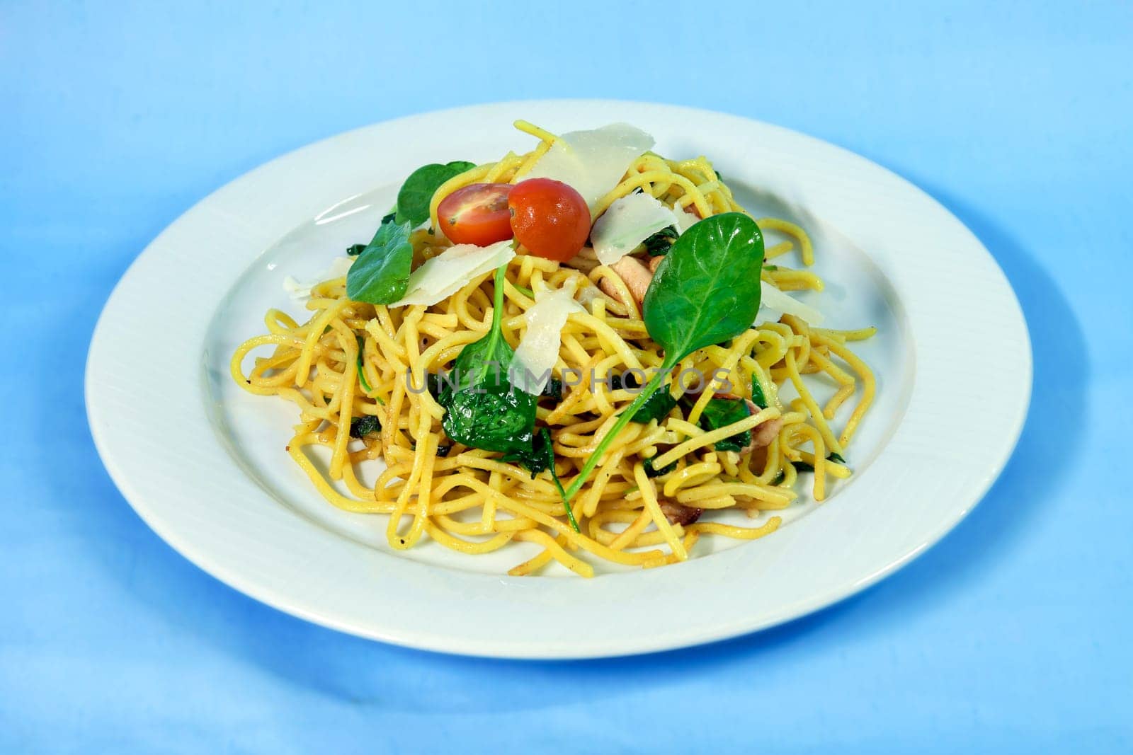 Modern food on a white plate and blue background - spaghetti with salmon and spinach