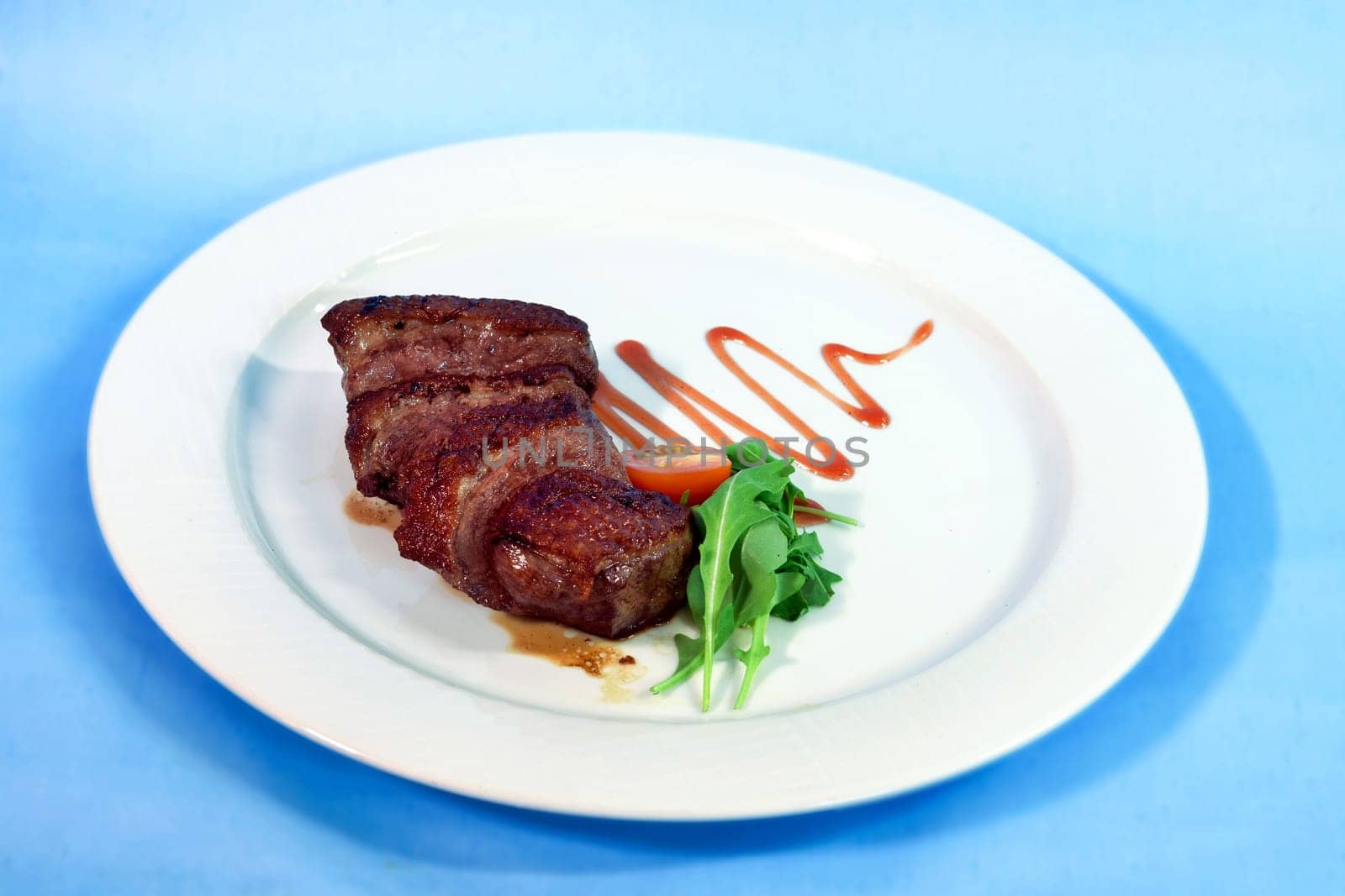 Modern food on a white plate and blue background - grilled duck breast with wine sauce