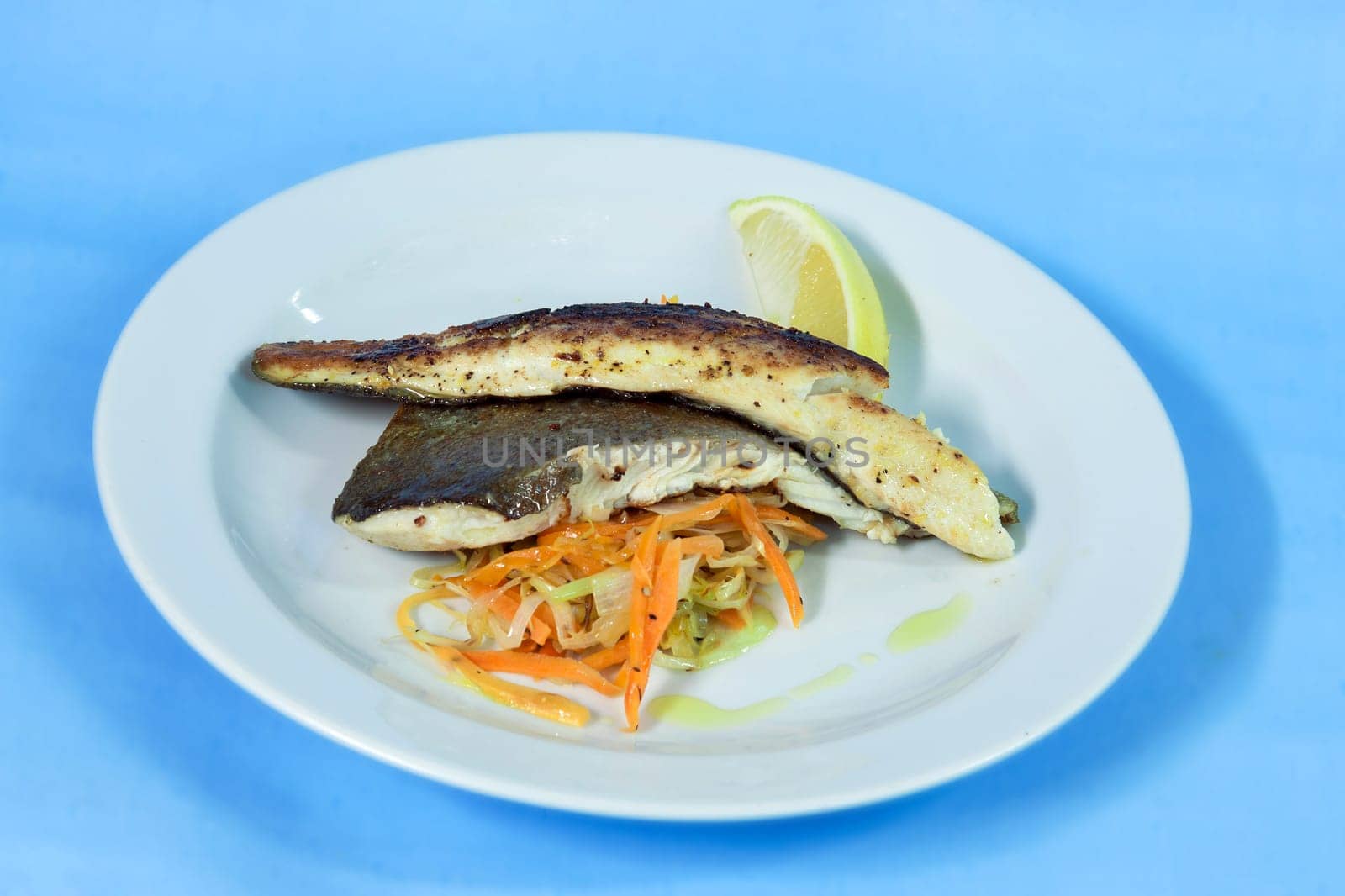 Modern food on a white plate and blue background - grilled boneless trout with roasted vegetables