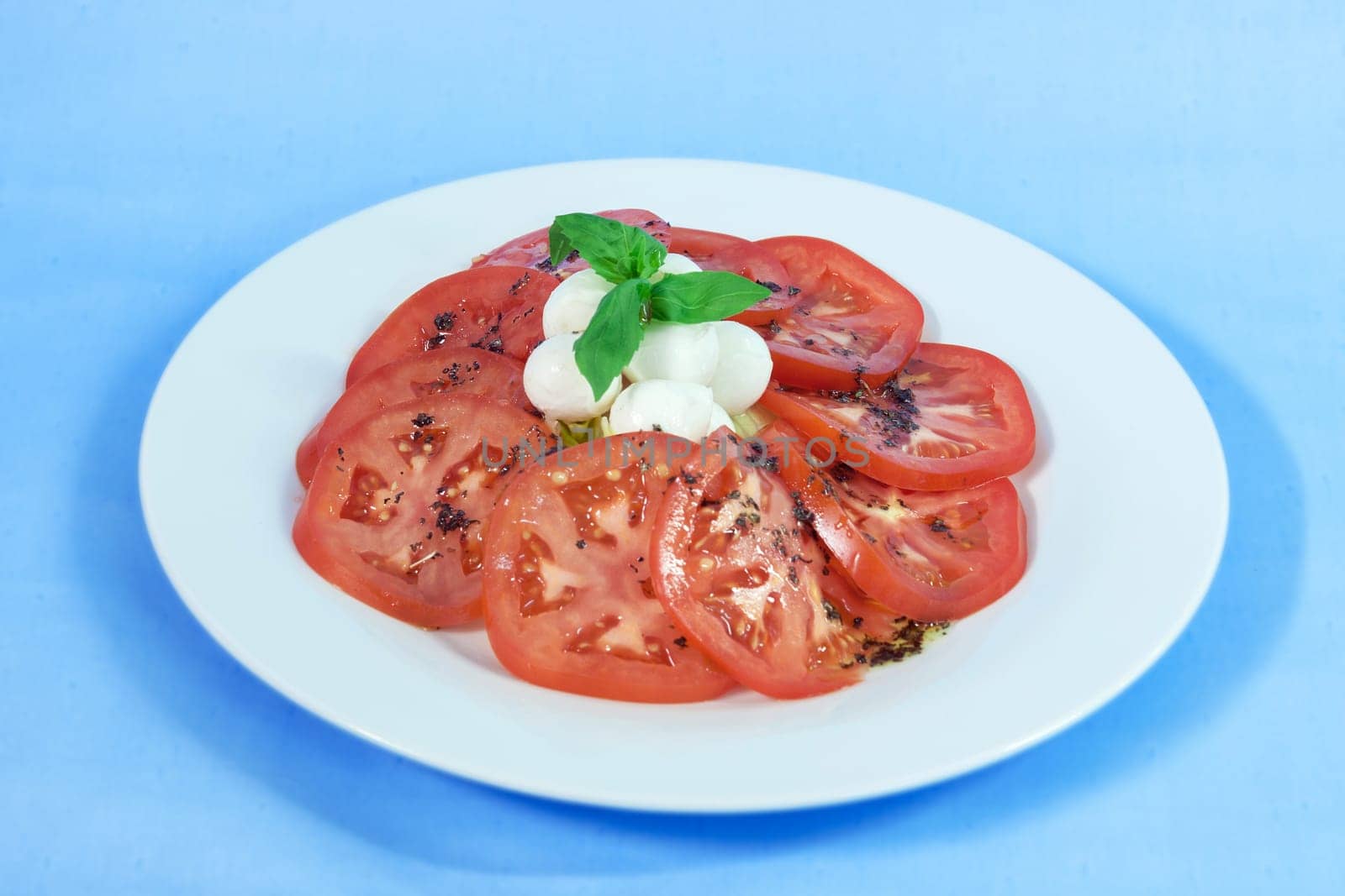 Modern food on a white plate and blue background - tomatoes with mozzarella and basil - caprese salad