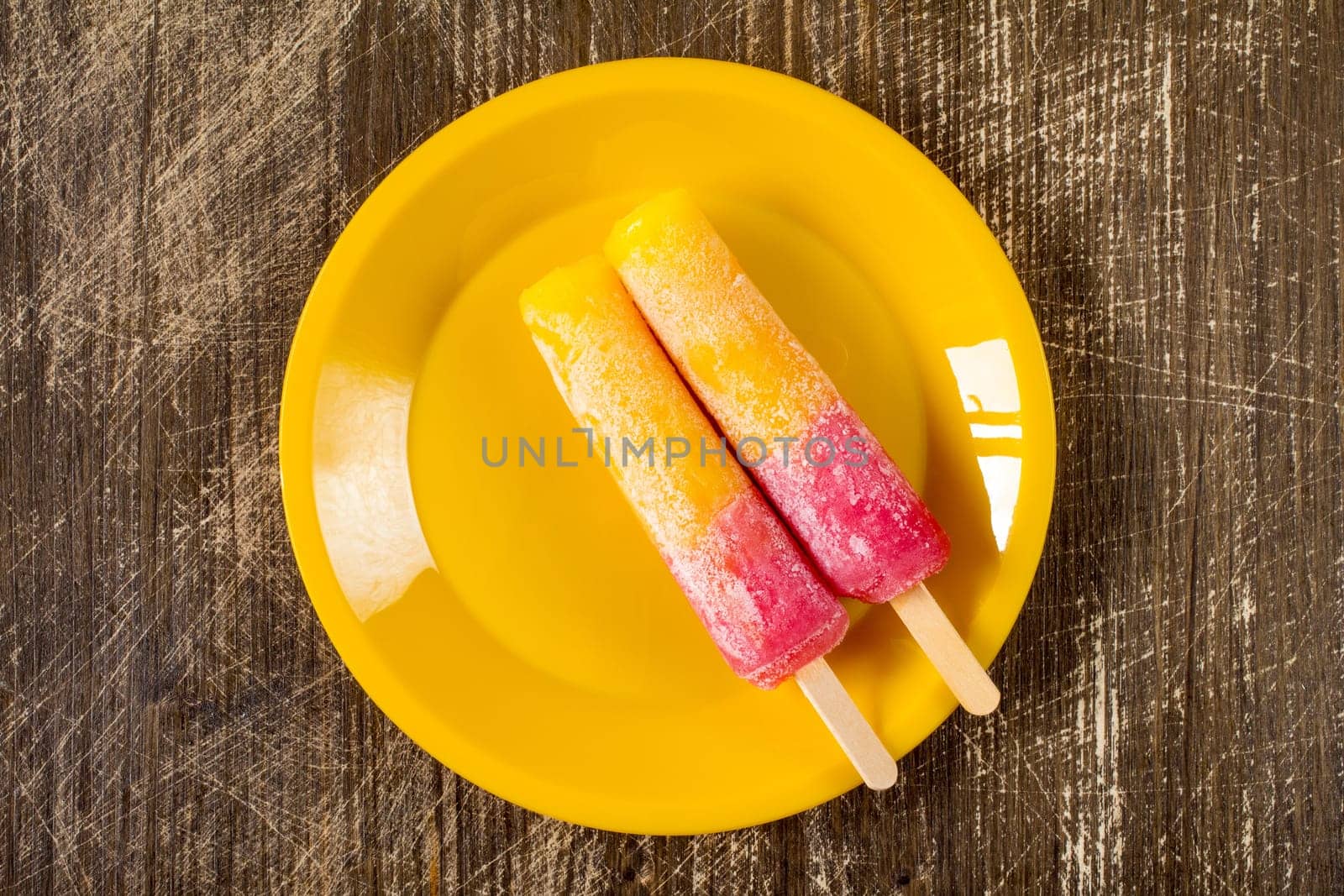 Two  Raspberry and Orange ice pops on a yellow plate