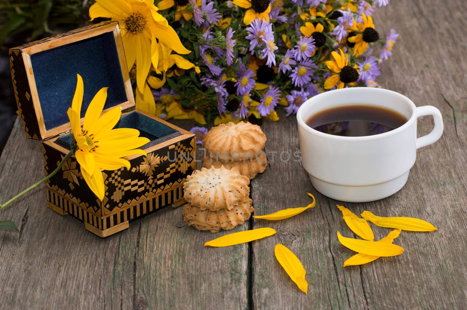 open casket, coffee, cookies, petals and wild flowers on an old table, a still life, a festive card, a greeting card, a subject drinks and flowers