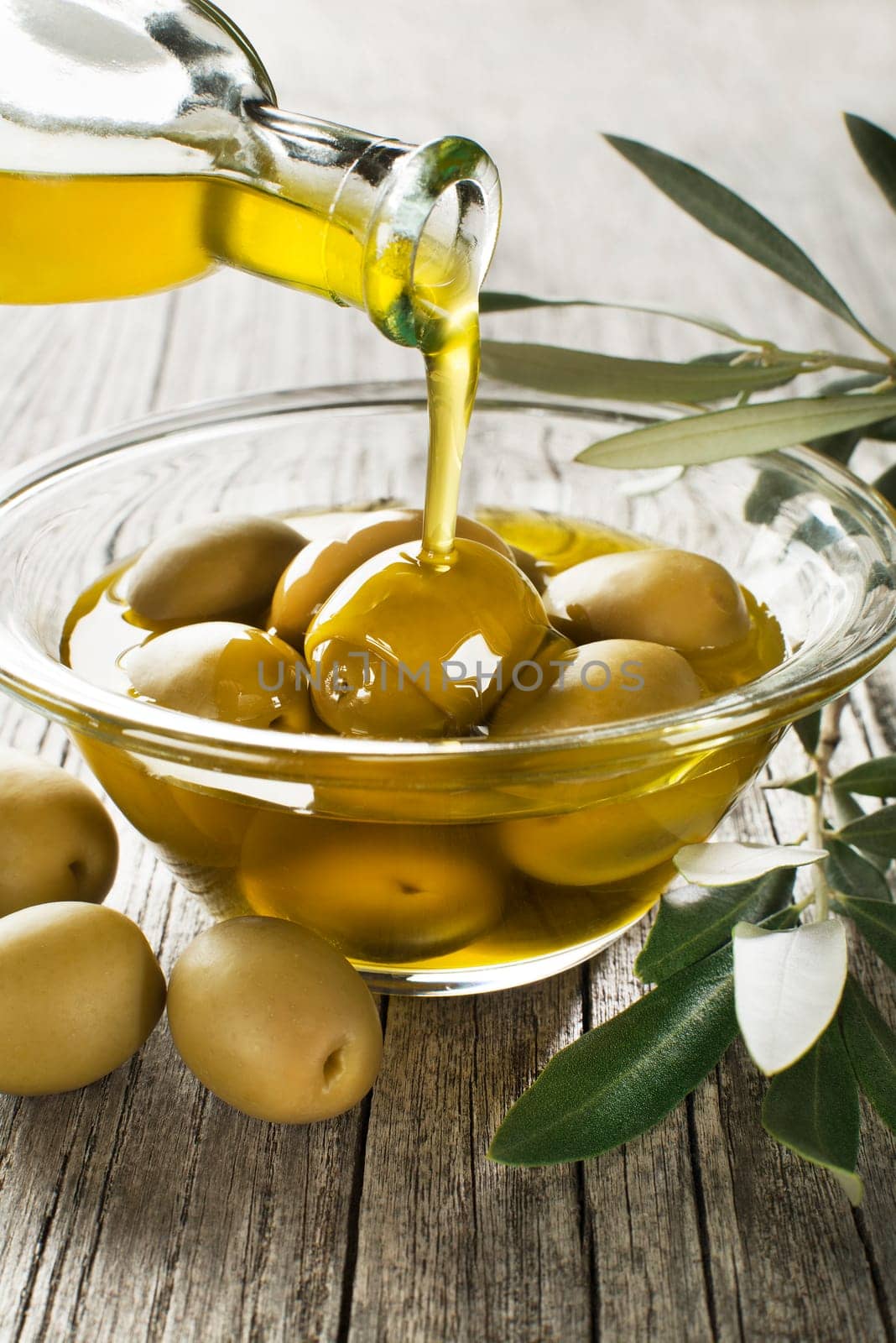 Bottle pouring virgin olive oil in a bowl with green olives close up