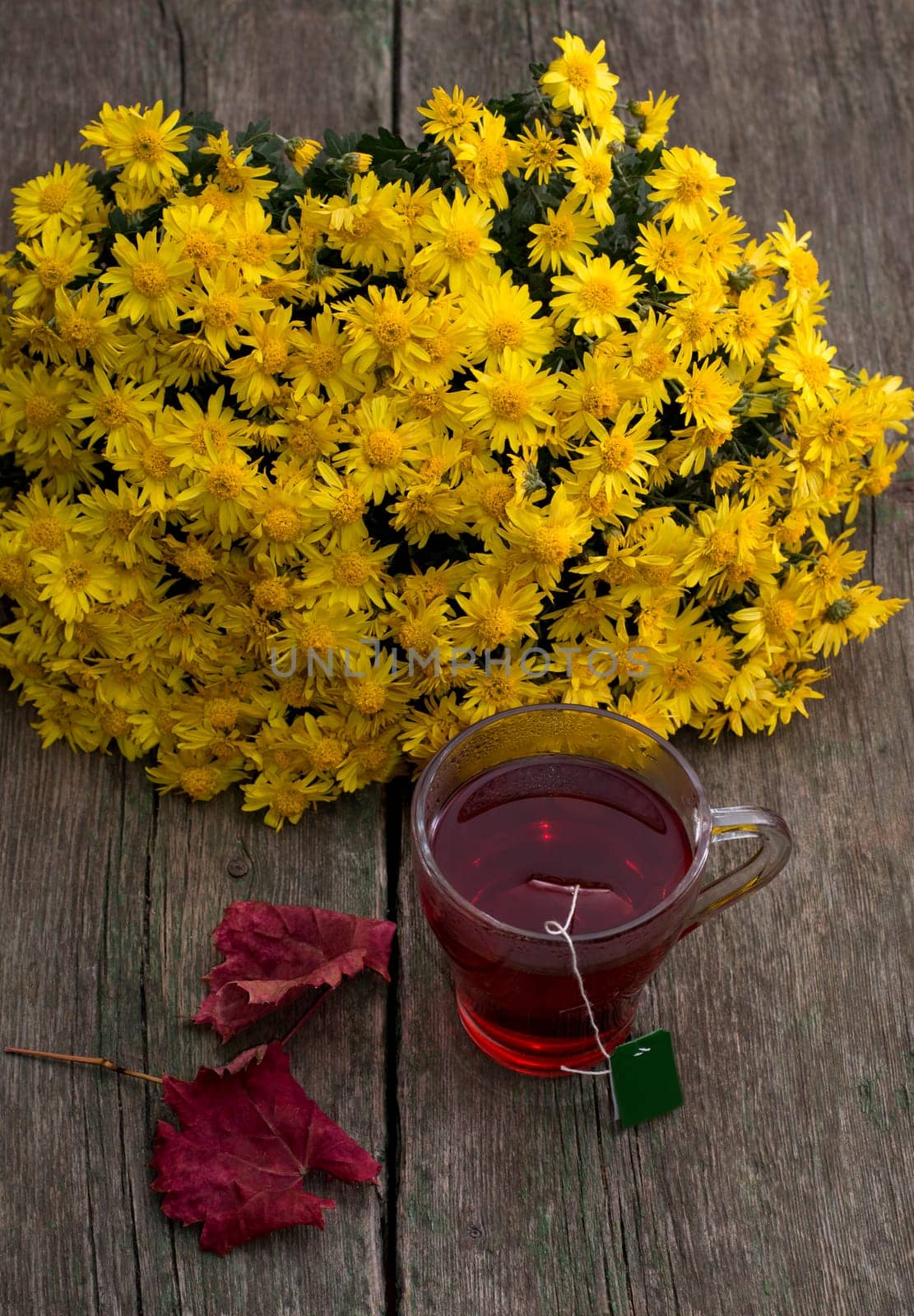 still life, bouquet of yellow flowers, transparent cup of tea and red leaf, on a wooden table, fall, a subject drinks
