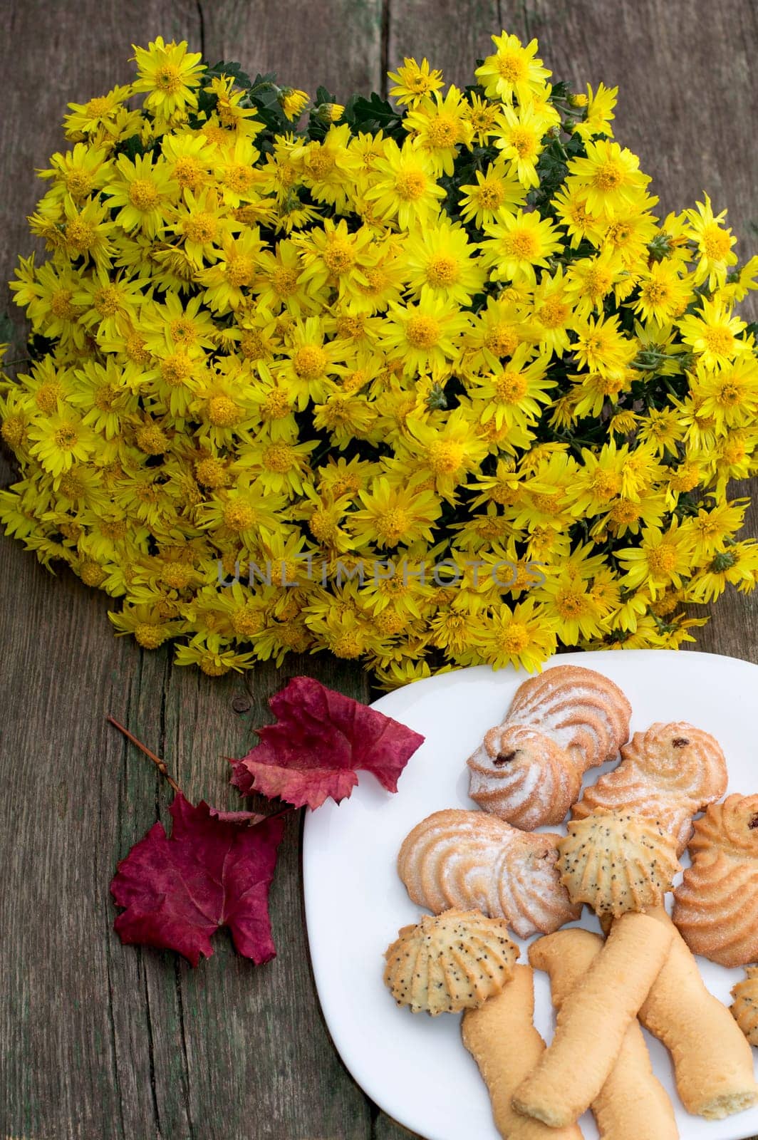 bouquet of yellow flowers, red leaf and plate with cookies, on a wooden table, fall a still life, a subject of sweet and flowers