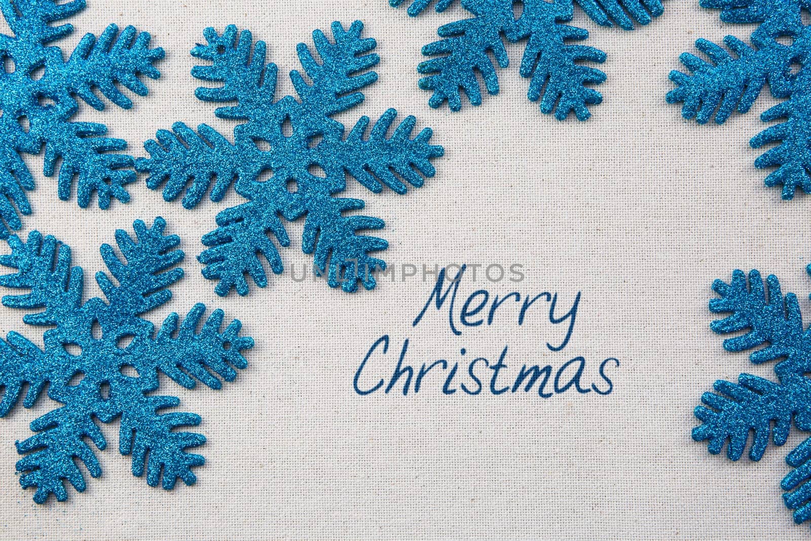 Sparkling blue snowflake ornaments on linen surface with Merry Christmas greeting.