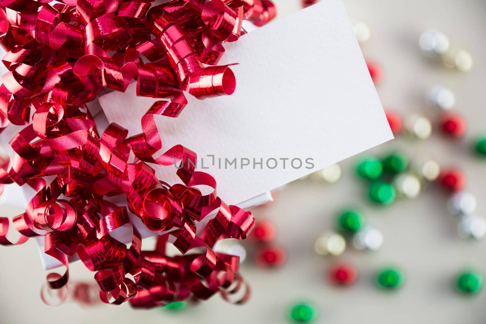 Red curly ribbons on gift box and gift tag with copy space, onaments out of focus in background.