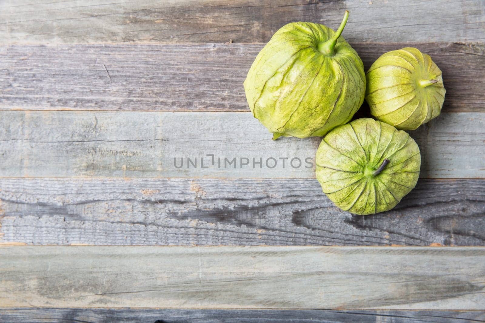 Three tomatillos on wooden surface with copy space.