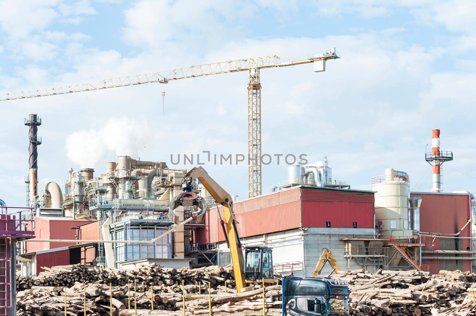 industrial plant of a furniture factory with smoking smokestacks,tubes,silos,crane ,truck and trunks.