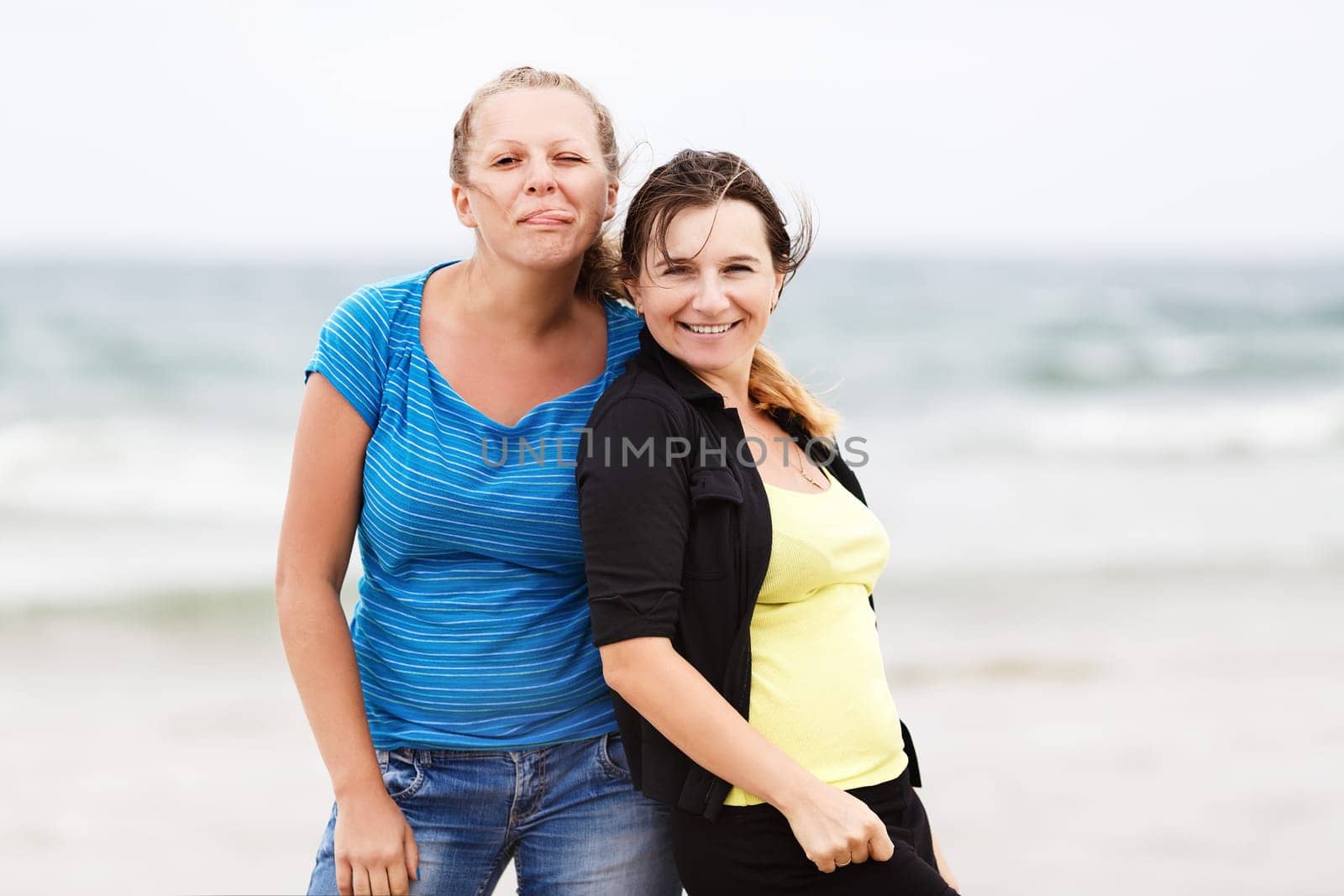 Two cheerful young women outdoors. Happy girls posing with pleasure show tongue and smiling.