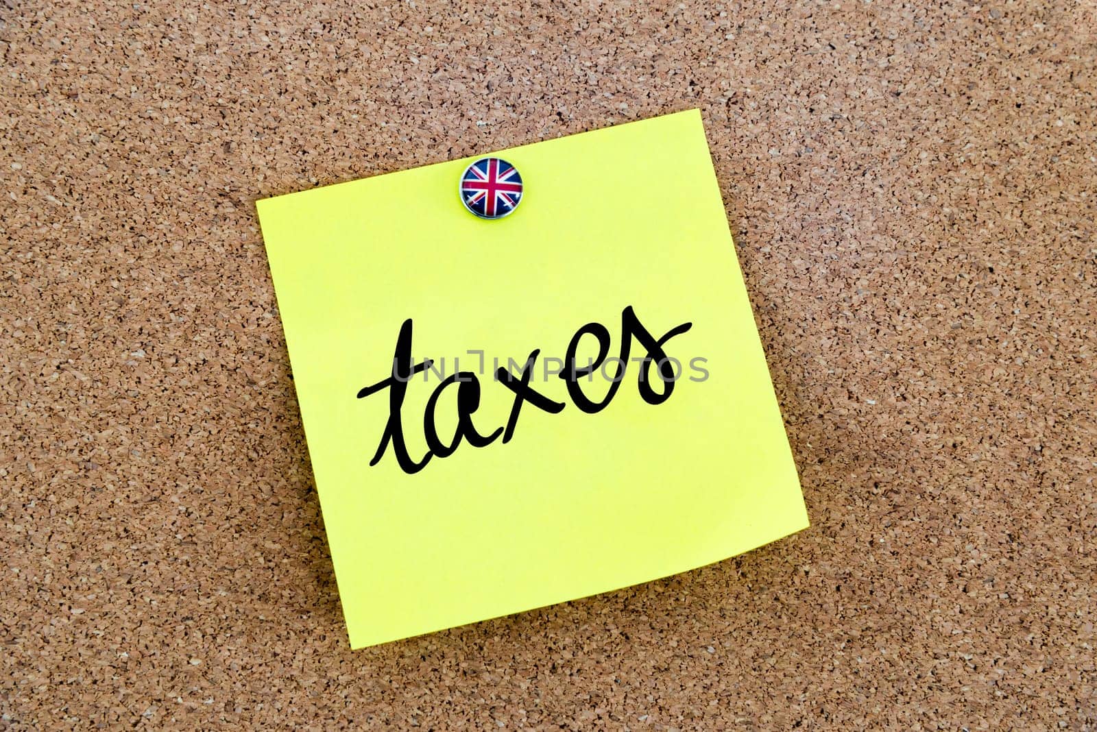 Yellow paper note pinned on cork board with Great Britain flag thumbtack, written text TAXES, United Kingdom exit from European Union concept