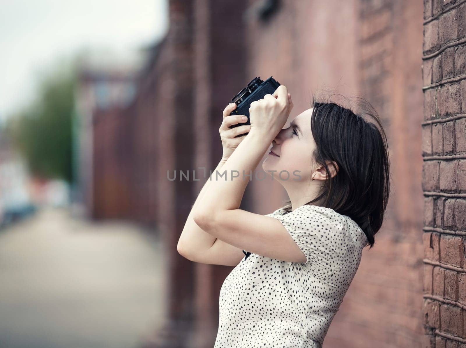 Pretty young woman taking photo outdoors. Girl holding vintage camera and taking photographs. Retro style photo. Selective focus on woman. Toned photo with copy space.