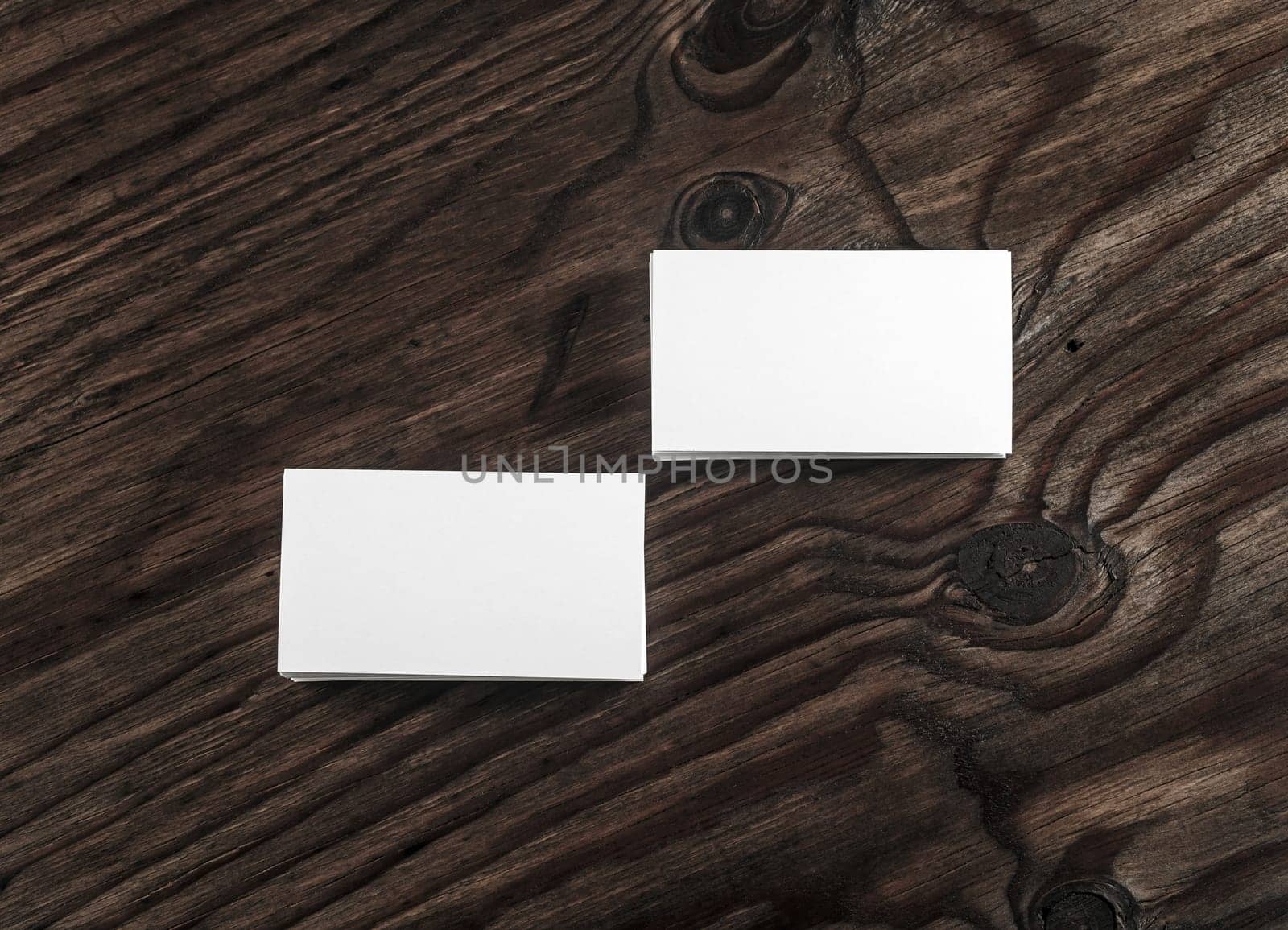 Blank white business cards on dark wooden table background. Mock-up for branding identity. Template for your design. Top view.