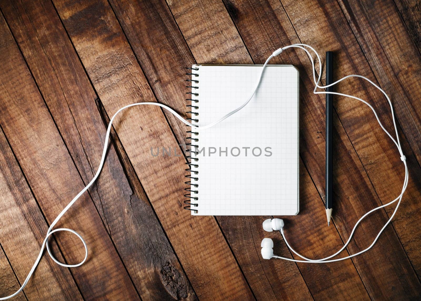 Blank notebook, pencil and headphones on vintage wooden table background. Blank paperwork mock-up for design portfolios. Top view.