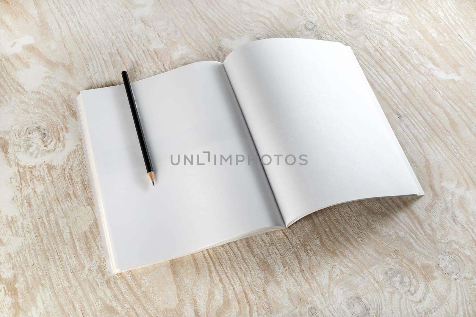 Blank opened brochure with a pencil on light wooden background with soft shadows. Template for design presentations and portfolios. Top view.