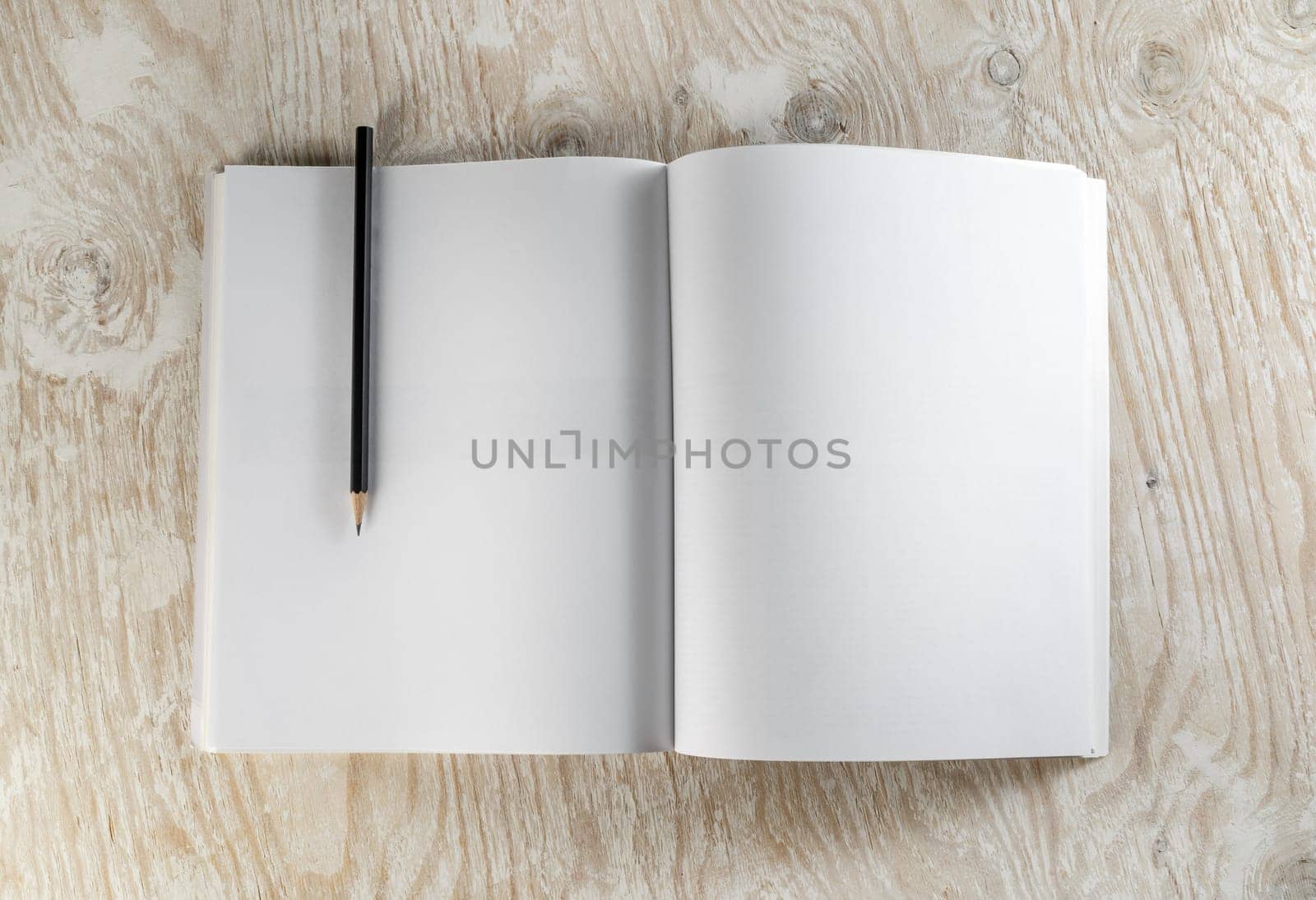 Blank opened brochure with a pencil on light wooden background with soft shadows. Template for design presentations and portfolios. Top view.