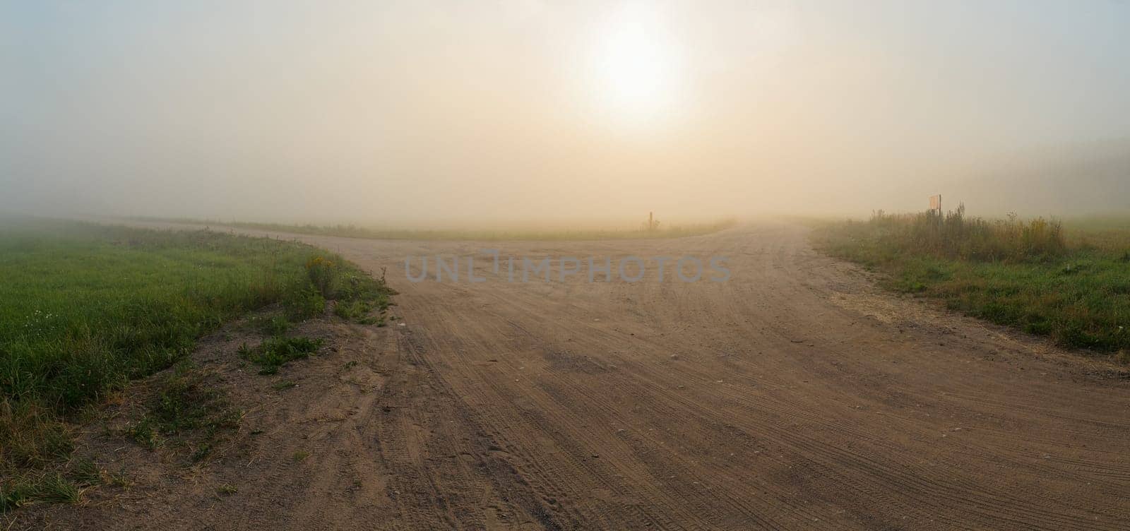 Landscape with an old gravel rural road in the fog. Panoramic shot. Toned image.