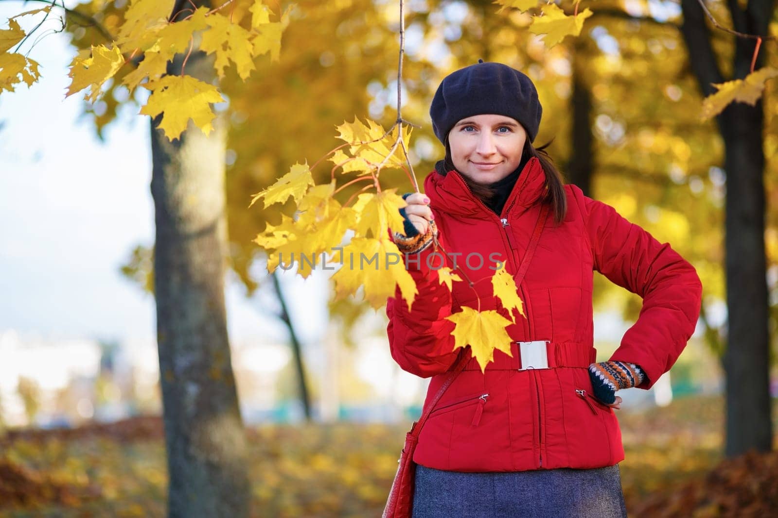 Woman in a beret and red jacket in the autumn park. Girl holding a maple branch with leaves in his hand. Selective focus on model.